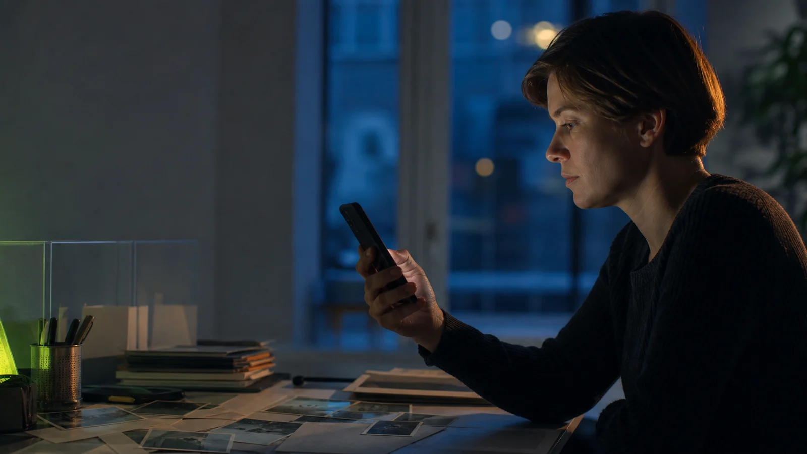 An anonymous person reviews contact clues at a desk while holding a phone with its screen turned away.