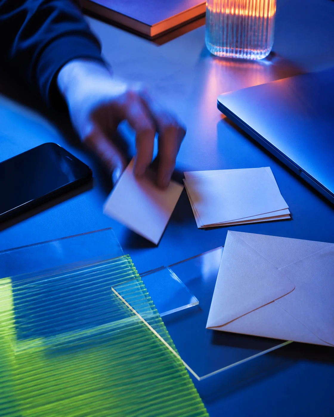 A hand moves among a dark-screen phone, blank cards, a laptop edge and translucent research layers.